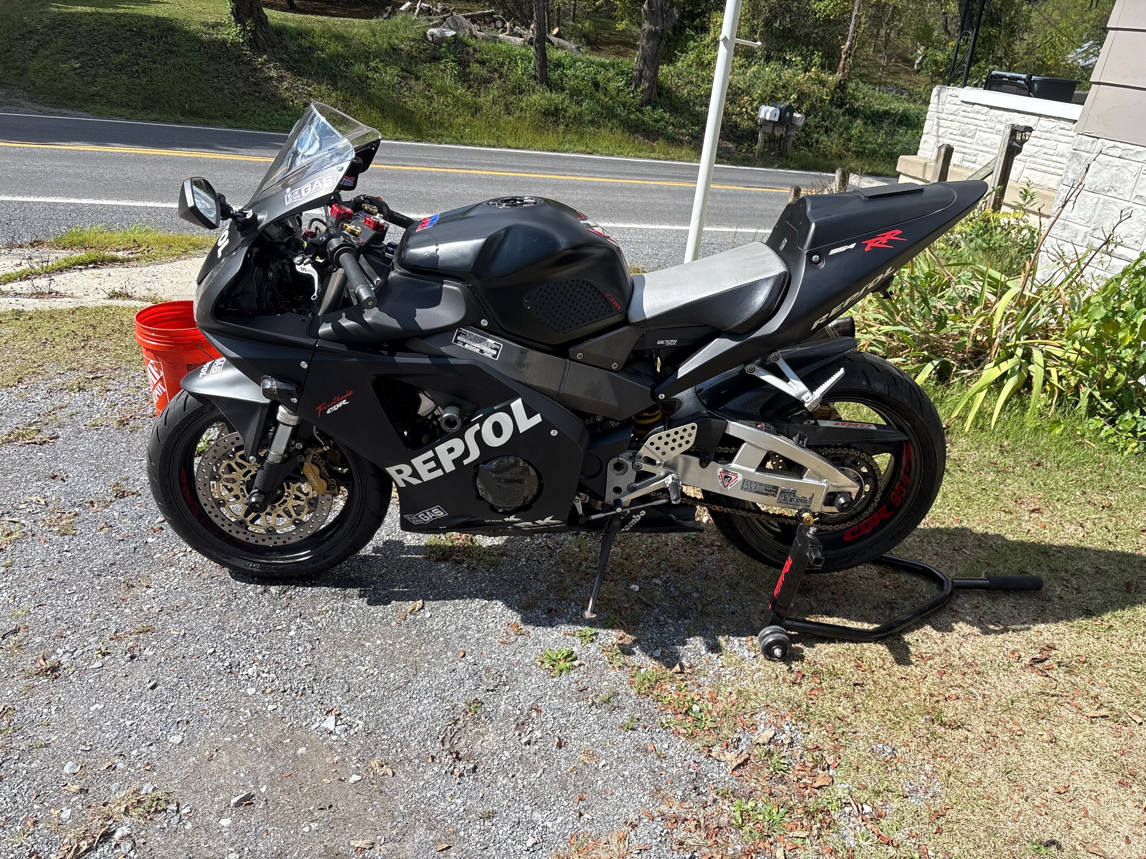 Matte black Repsol Honda sportbike parked on a gravel driveway next to a road.
